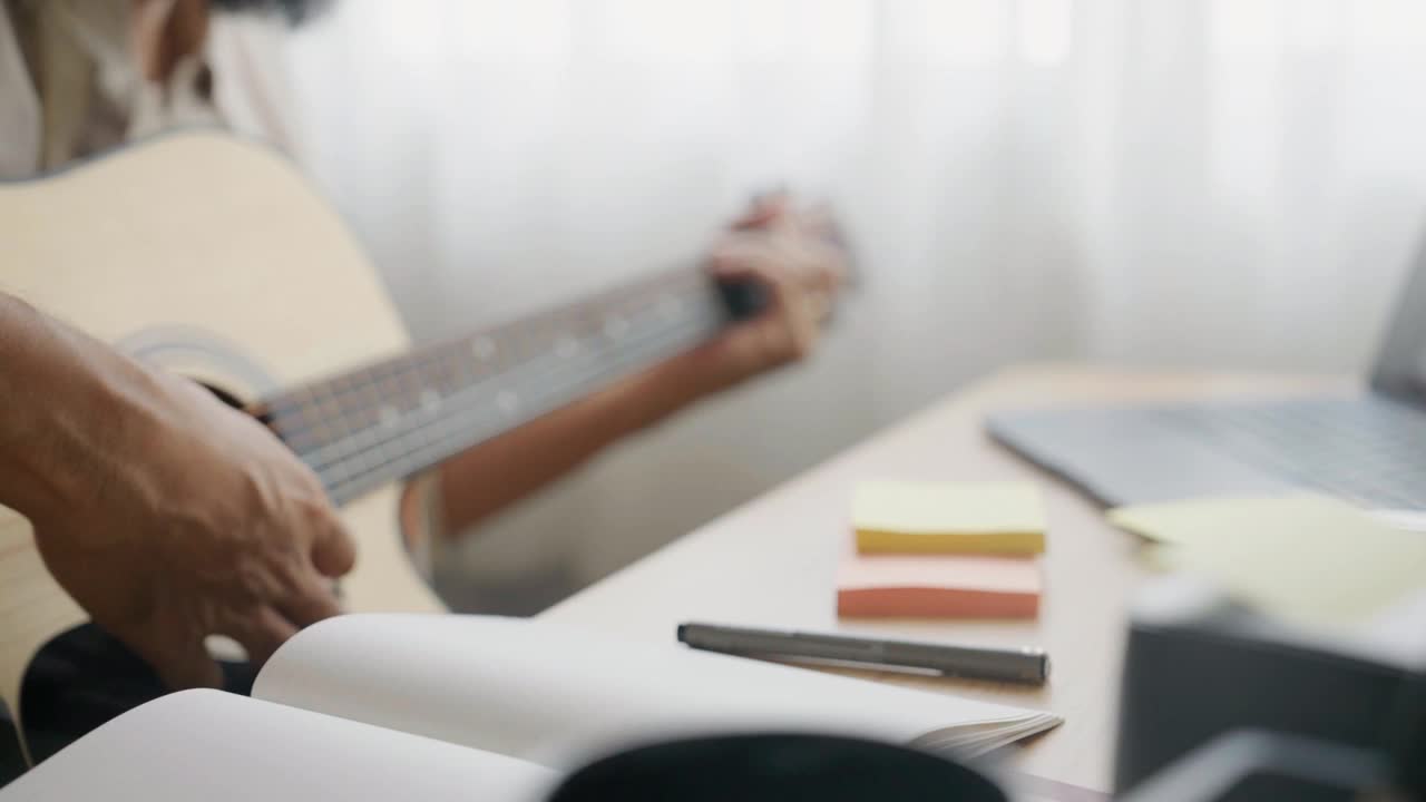 亚洲年轻艺人在家直播音乐。艺术家在家里的录音室里对着麦克风弹着原声吉他唱歌。视频下载