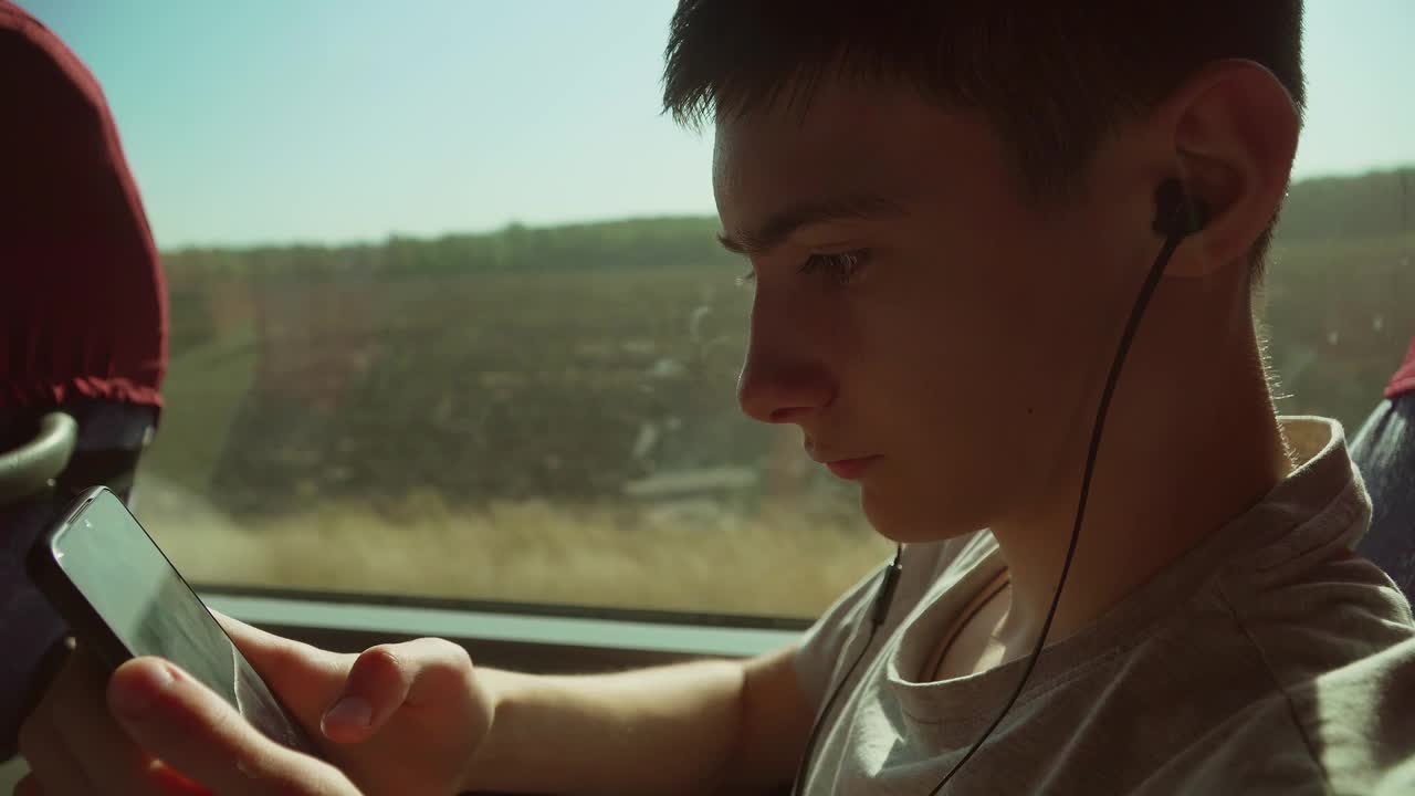 孩子用手机上网聊天，在公交车上看视频。十几岁的男孩在火车上戴着耳机。旅游生活方式交通视频素材