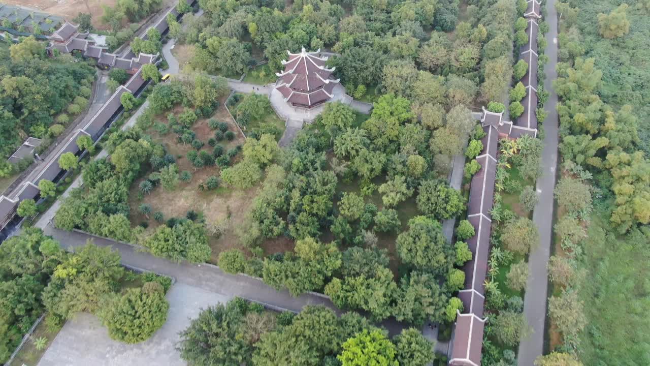日落时，无人机在越南宁平一条蛇河前的一个长满绿树的佛教寺庙上空飞行视频素材