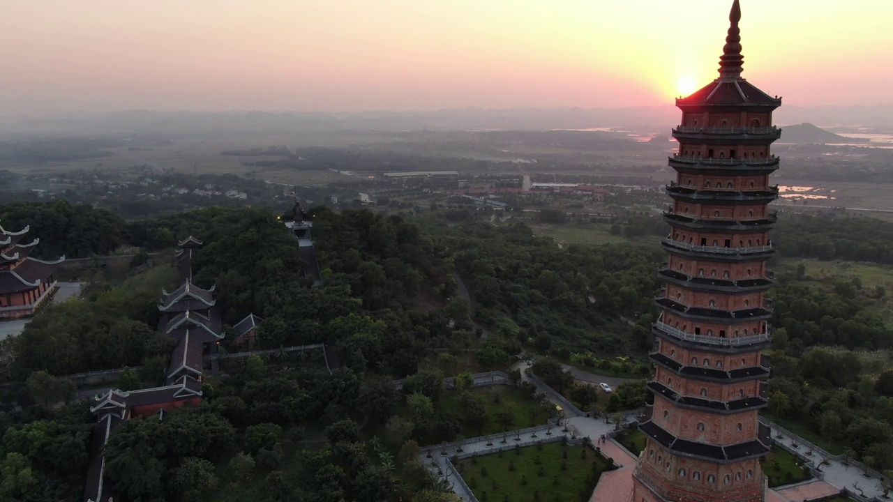 夕阳下，在越南宁平，一架无人机在布满绿树和宝塔的佛教寺庙上空飞行视频素材
