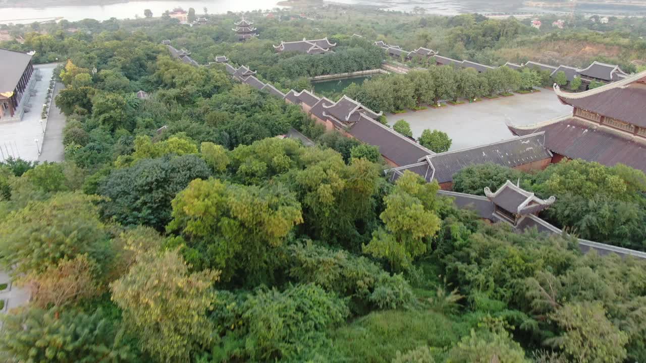 日落时，在越南宁平一条蛇河前，无人机在长满绿树的佛教寺庙上空飞行视频素材