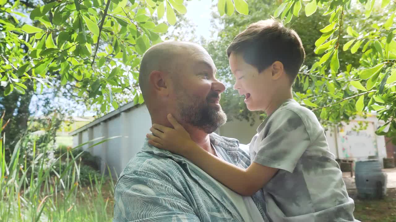 阳光明媚的一天，父亲带着患有唐氏综合症的儿子在花园里微笑视频下载