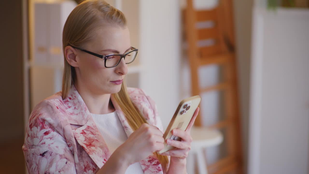 年轻的金发女商人正在浏览智能手机视频下载