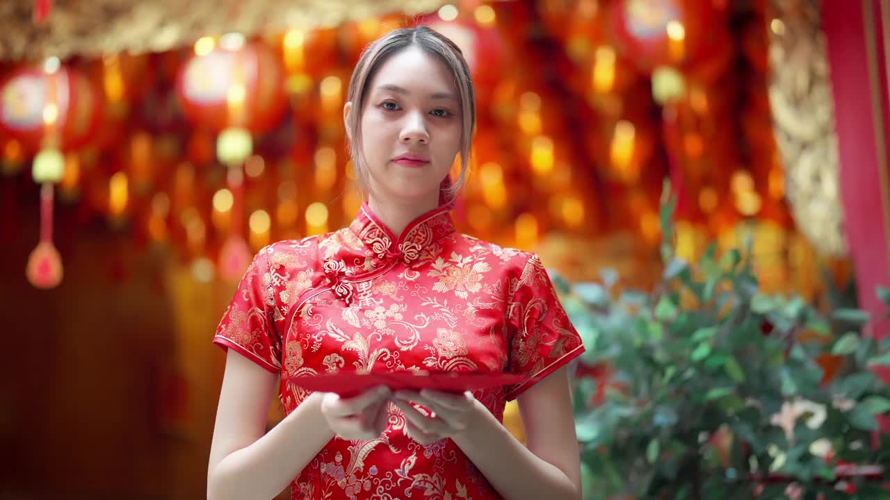 年轻的亚洲女孩穿着红色旗袍，手里拿着红包，在中国的寺庙里向空中递红包。给父母礼物或钱。视频下载