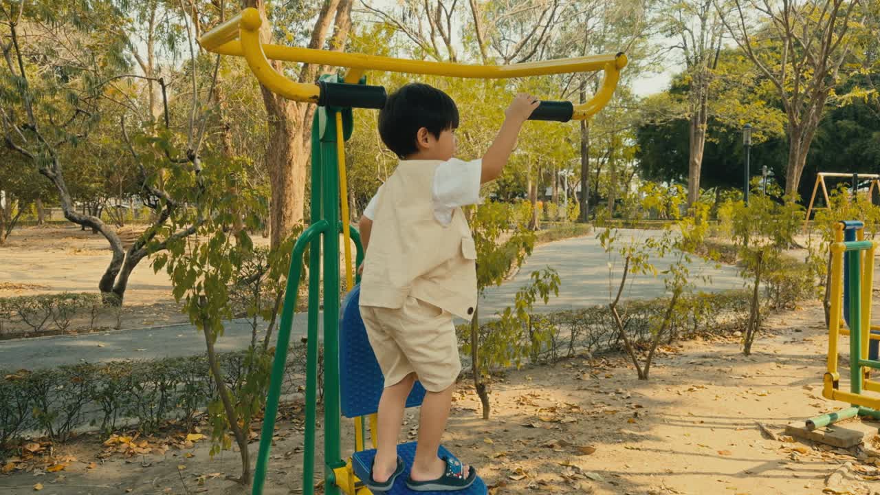 在操场上，一个亚洲小男孩微笑着在户外运动器材上玩耍。积极的生活方式。视频下载