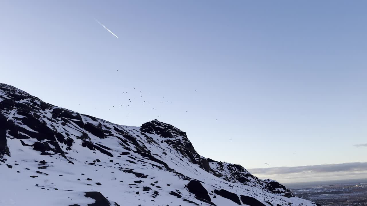 白雪覆盖的山坡，蓝天下的岩石地形视频下载