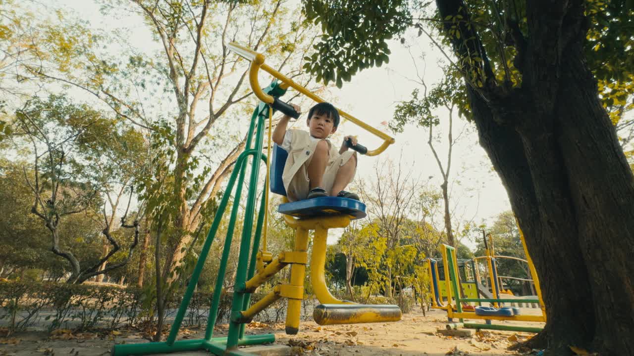 在操场上，一个亚洲小男孩微笑着在户外运动器材上玩耍。积极的生活方式。视频下载