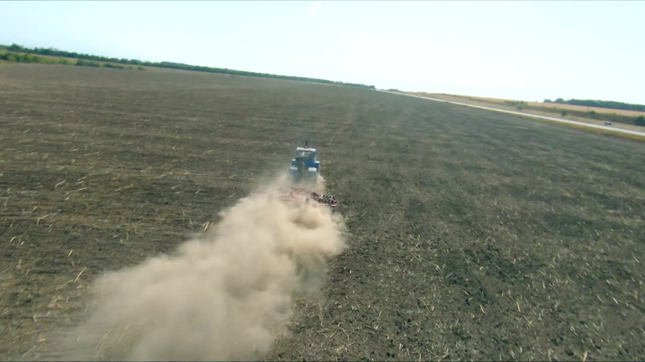 用耙制拖拉机在耕地上犁地的航拍照片。收获后处理田地，后面有一柱灰尘。农业机械驶过农田视频下载