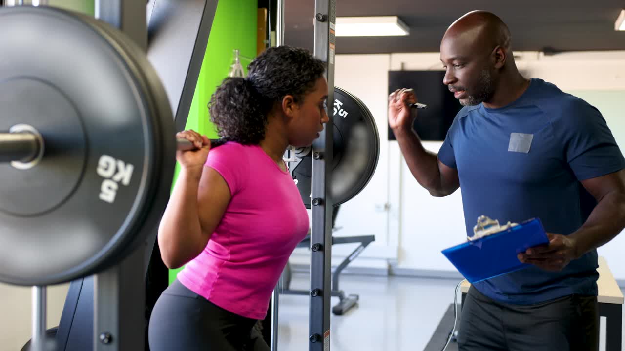非裔美国男教练在健身房向年轻女子解释举重时如何分配重量视频下载