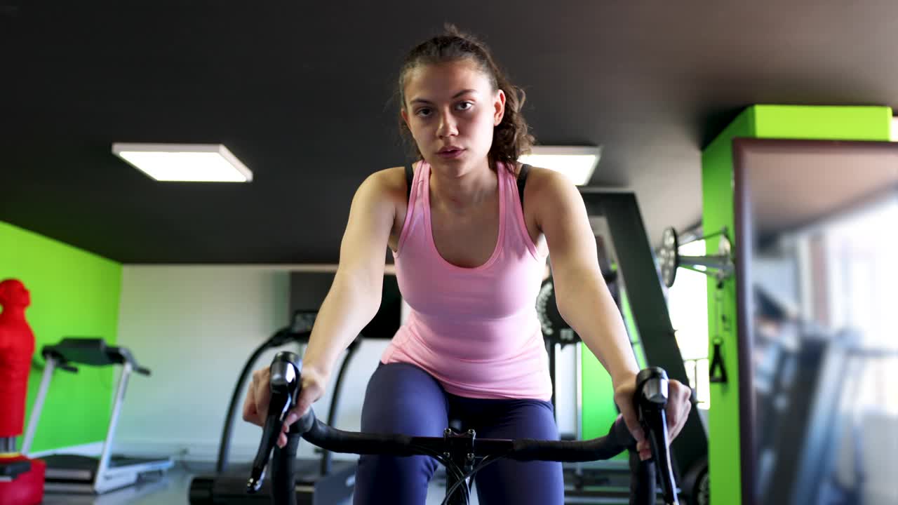 年轻女子在家里的固定自行车上训练视频下载