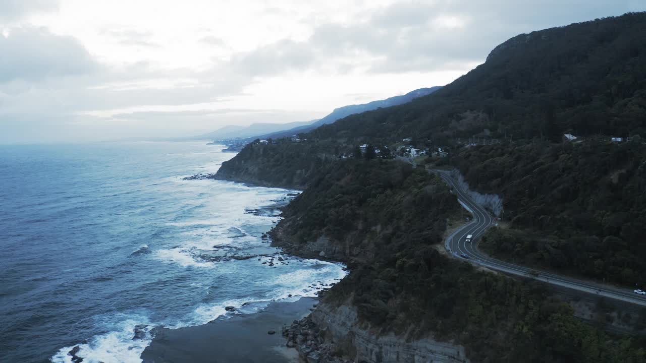 空中锁定汽车在山间公路上行驶的美丽景色，波浪般的大海-卧龙岗，澳大利亚视频素材