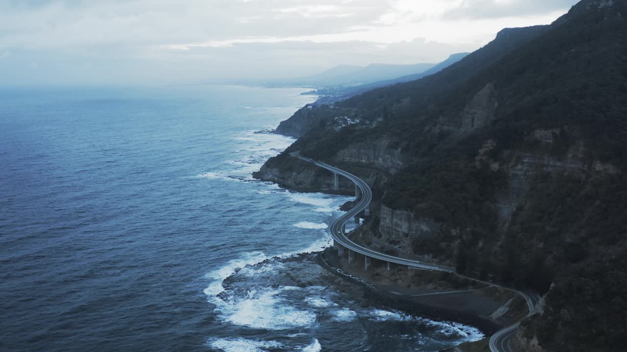 在宁静的岩层中俯瞰著名的海崖桥，无人机在波涛汹涌的海面上向前飞行——澳大利亚卧龙岗视频下载