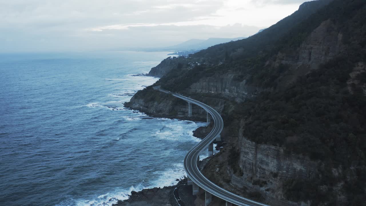 空中拍摄的蜿蜒道路的海崖桥由山，无人机向前飞行在波涛汹涌的海洋-卧龙岗，澳大利亚视频素材