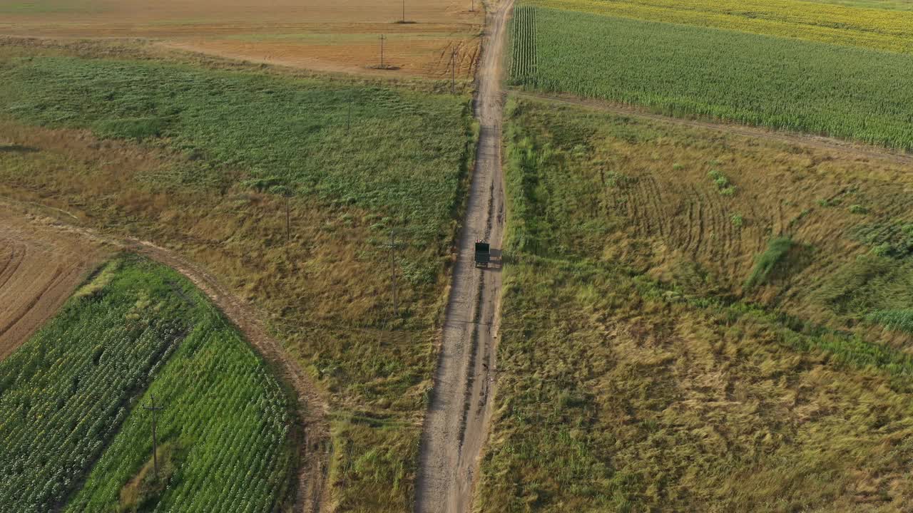 夏日里，农用拖拉机拖着空货车行驶在乡间的土路上，在地上投下阴影，无人机拍摄的航拍画面视频下载