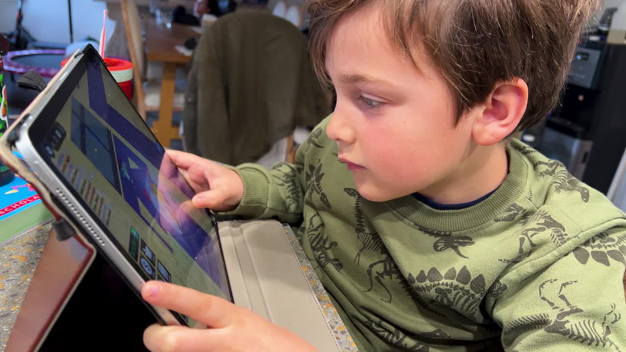 快乐的小男孩在自家厨房用他的数码平板电脑玩电子游戏视频下载