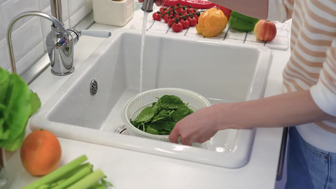 塑料碗里的菠菜在水槽里用自来水冲洗。健康沙拉的配料视频下载