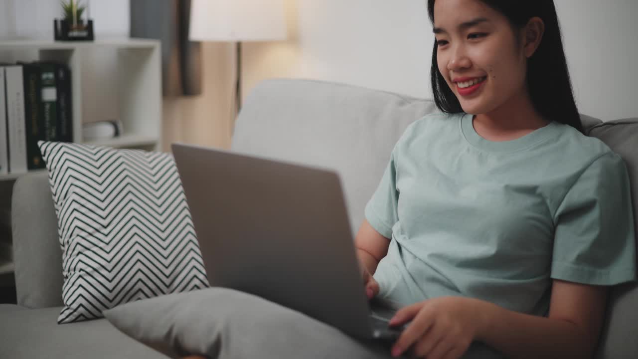 年轻女子在家里的沙发上用笔记本电脑上网购物。视频下载