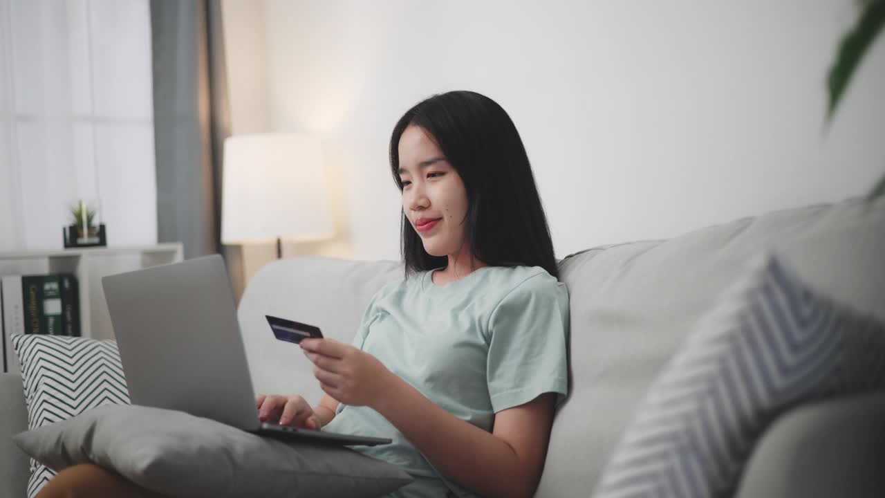 年轻女子用笔记本电脑和信用卡在家里的沙发上网购。视频下载