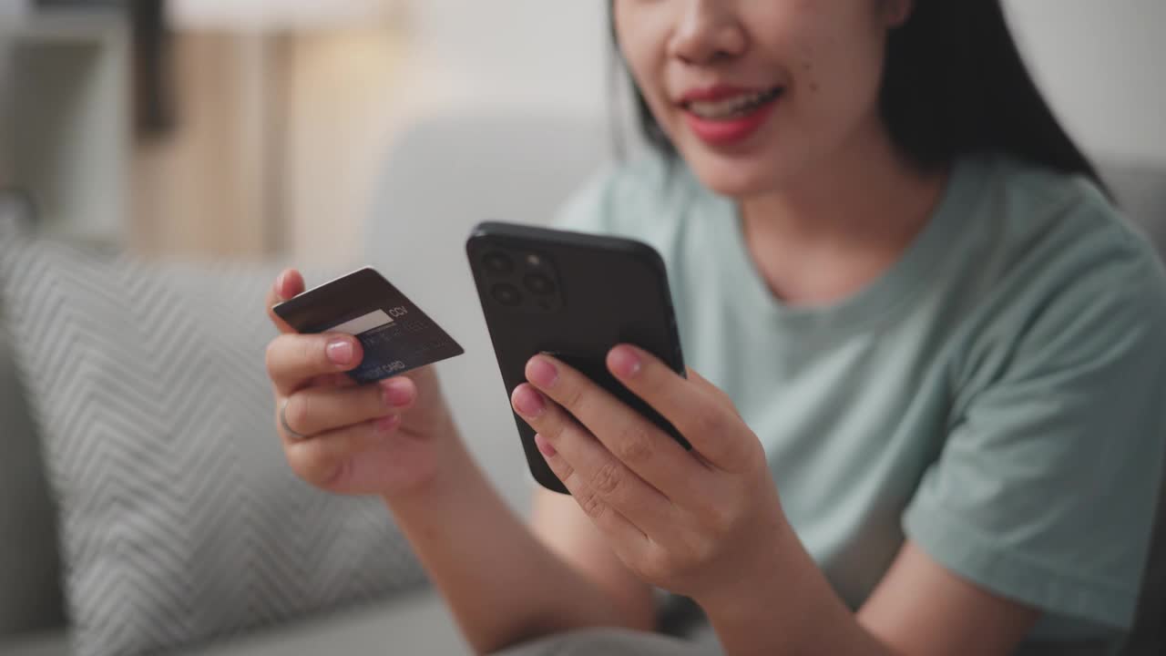 年轻女子用手机和信用卡在家里的沙发上网购。视频下载