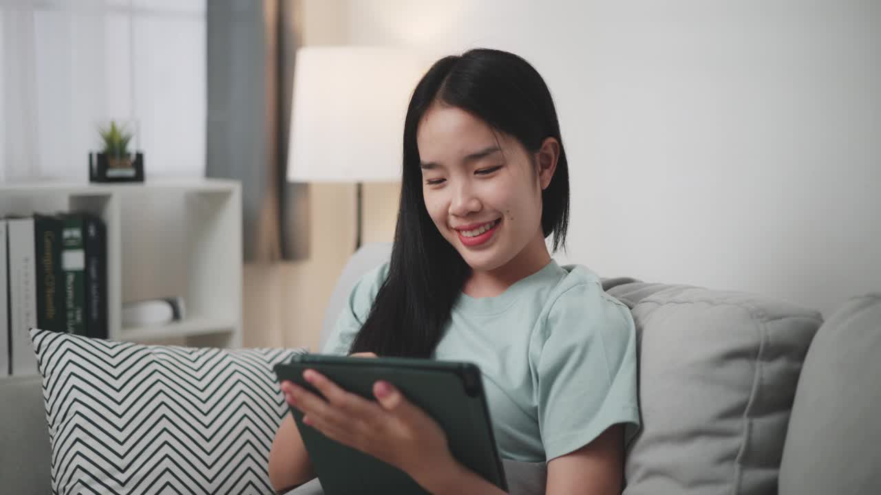 年轻女子在家里的沙发上用平板电脑上网购物。视频下载