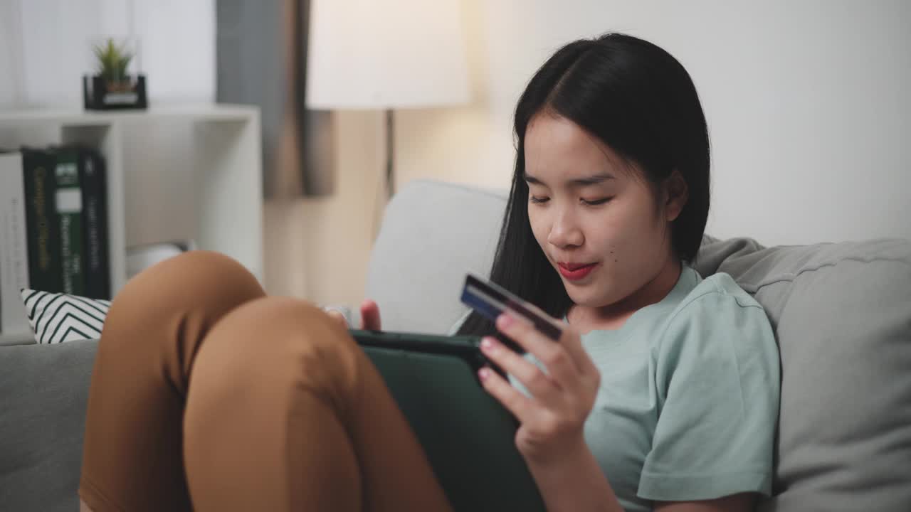 年轻女子用平板电脑和信用卡在家里的沙发上网购。视频下载