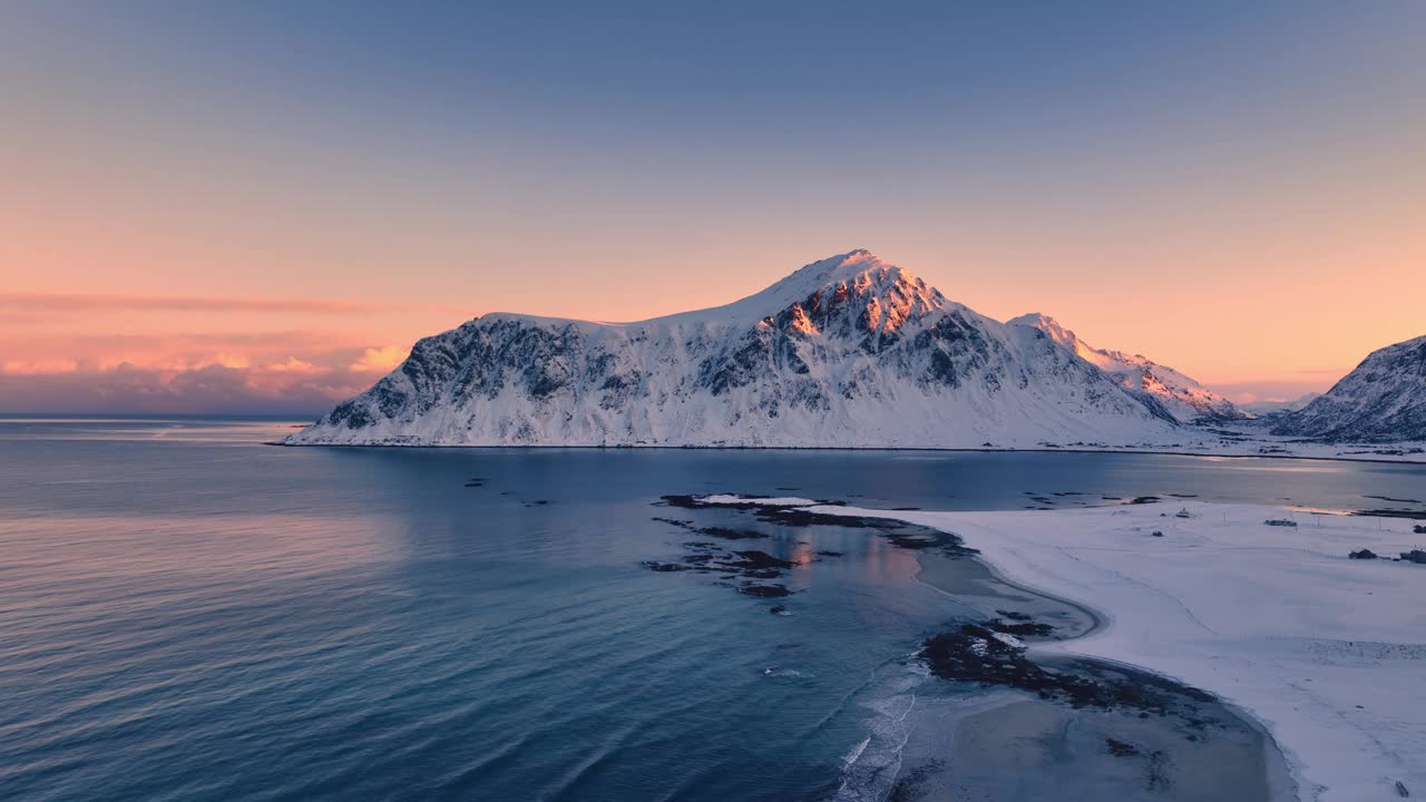 挪威罗弗敦群岛乌塔克莱夫海滩的冬季景观，冰雪覆盖的山峰，岩石海岸线和风景秀丽的日落，航拍4K视频视频下载