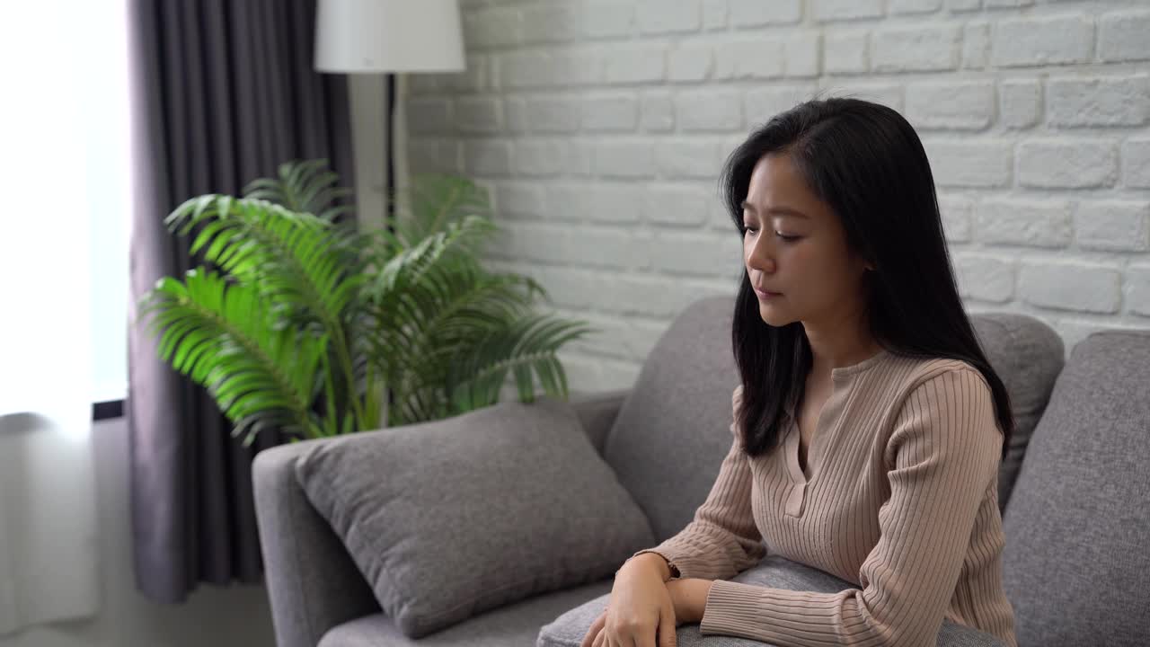 亚洲女性坐在家里的沙发上感到压力视频下载