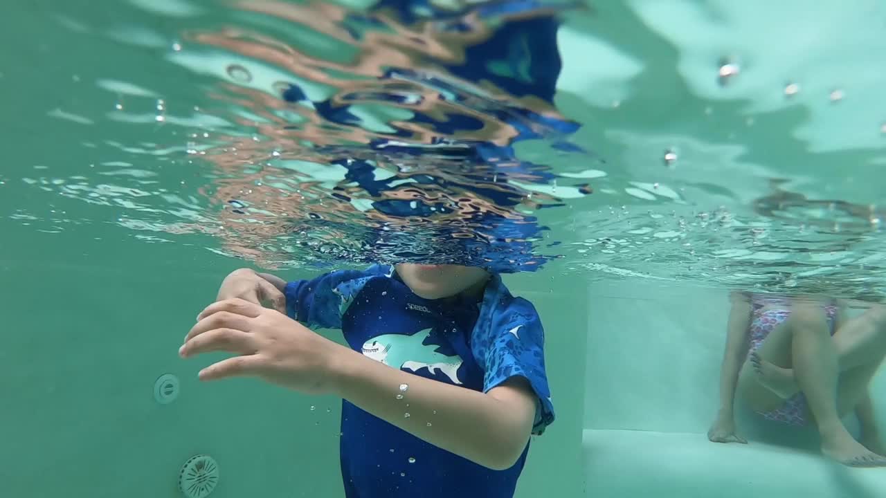 可爱的男孩在游泳池里蹦蹦跳跳，水面洒满阳光视频下载