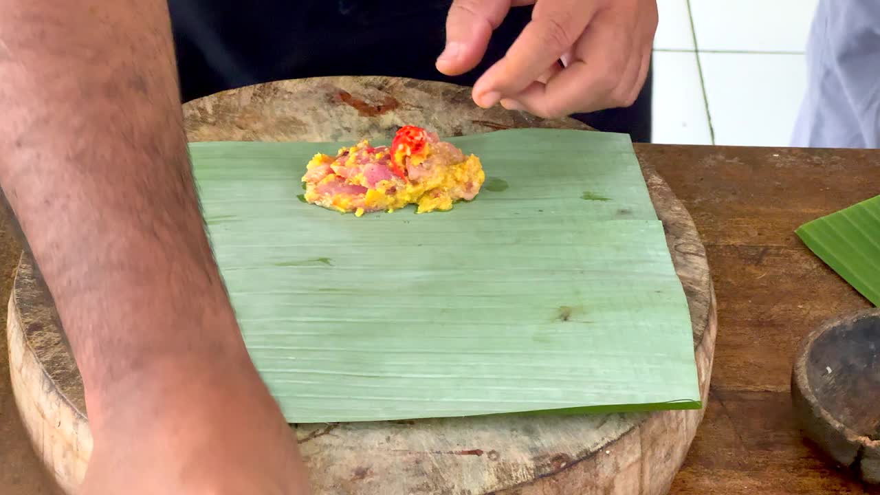 厨师将新鲜的辣椒和罗勒叶加入到生金枪鱼和香蕉叶上的其他食材中视频下载