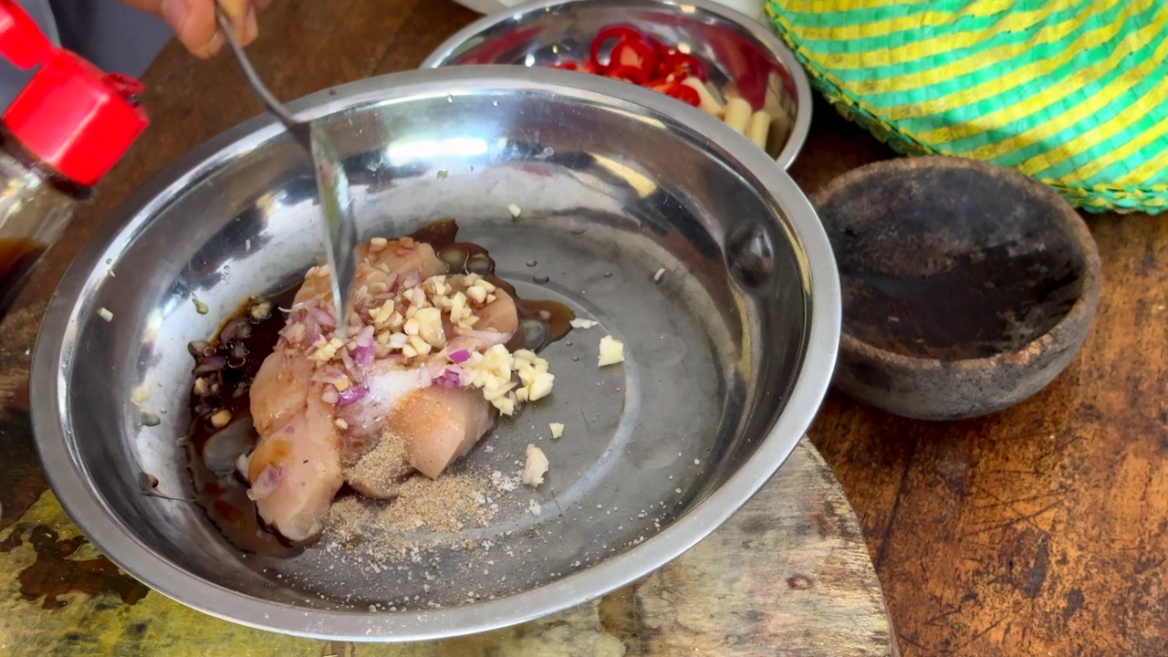 一名厨师在生鸡肉中加入浓稠的甜酱油、洋葱和大蒜，为美味的沙茶鸡肉串调味，这是巴厘岛传统烹饪的一部分视频素材