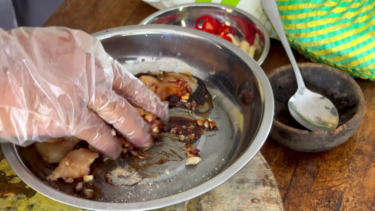 一名厨师用戴着手套的手将酱油、香料和调味料混合到生鸡肉中，同时烹饪传统的巴厘岛沙茶鸡肉串。视频素材