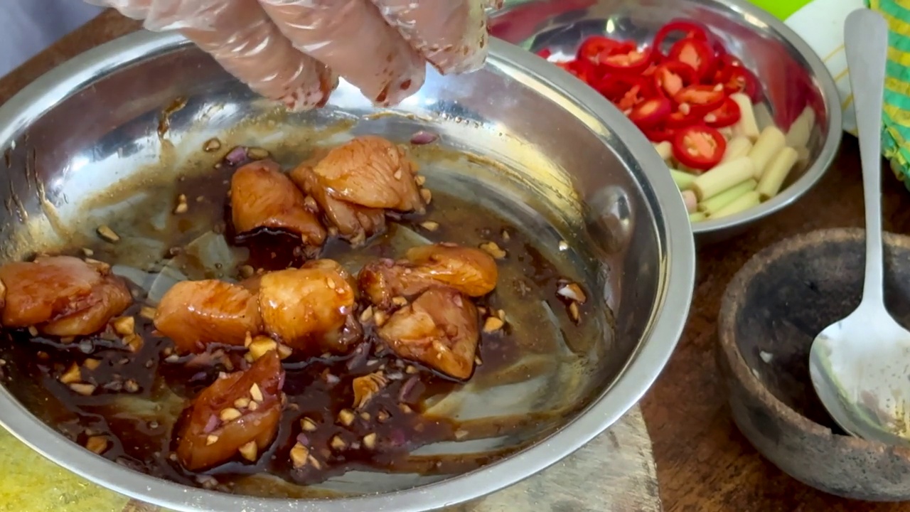 一名厨师用戴着手套的手将酱油、香料和调味料混合到生鸡肉中，同时烹饪传统的巴厘岛沙茶鸡肉串。视频下载
