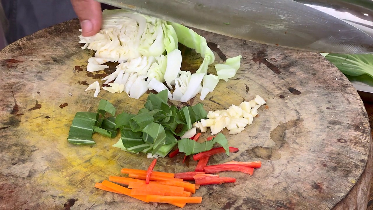 厨师熟练地用一把大刀在木制砧板上切碎新鲜的卷心菜，准备做传统的亚洲炒菜视频下载