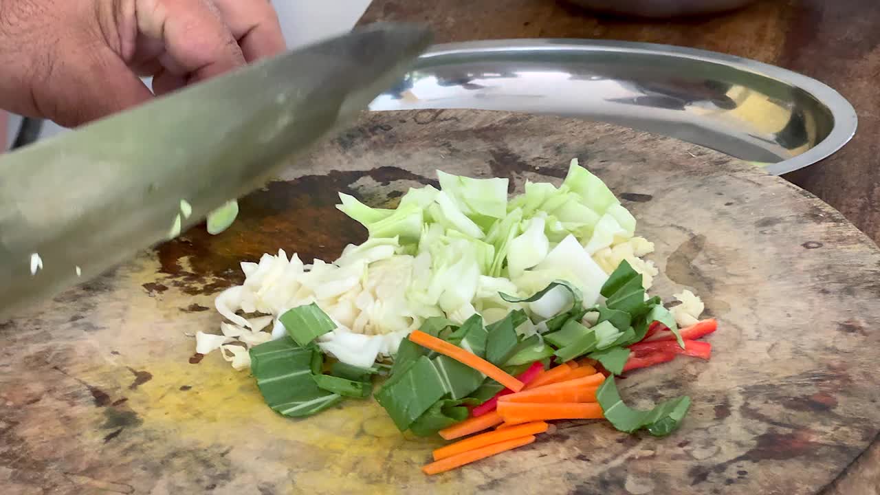 厨师熟练地用一把大刀在木制砧板上切葱花和青葱，连同其他食材一起做一道美味的亚洲炒菜视频下载
