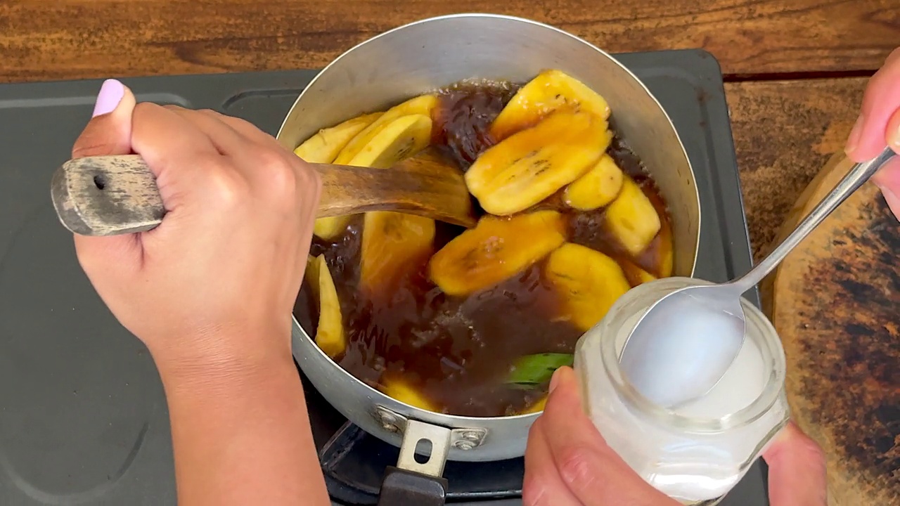 一起烹饪——一名厨师将椰奶倒入平底锅中，一名妇女在平底锅中搅拌大蕉和糖浆，准备一道传统的印尼甜点视频下载