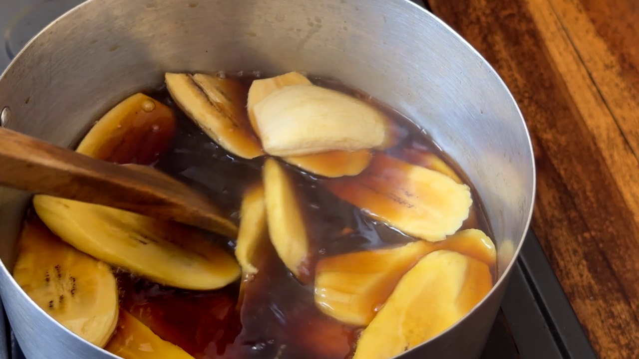 一位家庭厨师搅拌一个装满大蕉和糖浆的炖锅，准备一道传统的印尼甜点视频下载