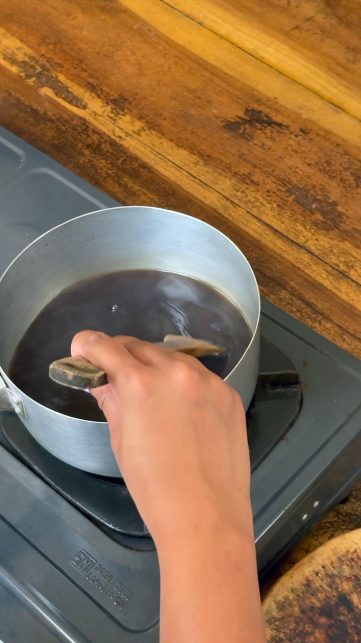 一名妇女在煤气灶上用木勺搅拌炖锅里的糖浆，制作美味的巴厘岛传统大蕉甜点视频下载
