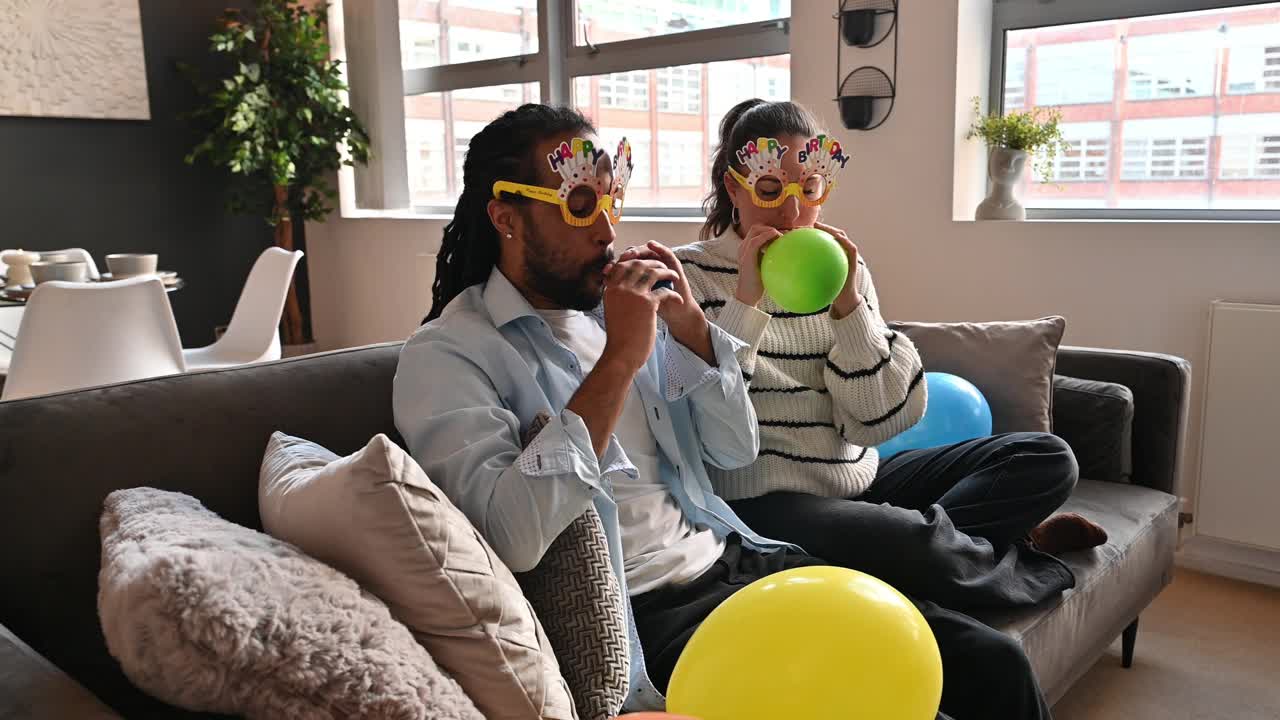 一对夫妇在家里庆祝生日。多种族夫妇吹气球，准备生日聚会视频下载