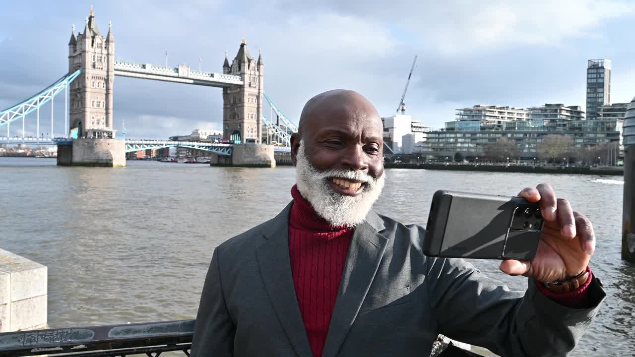 资深非洲裔商务旅行者在伦敦著名的塔桥附近。一位老年游客在伦敦地标附近自拍视频下载