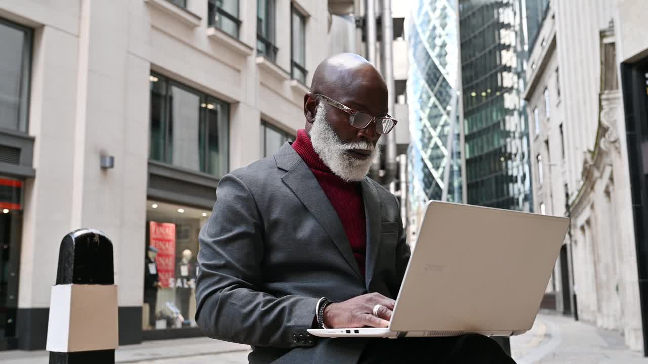 在金融区的加勒比裔成熟商人，在移动中使用笔记本电脑视频下载