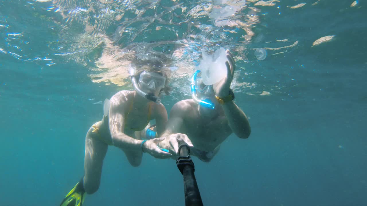 一对年轻的慢动作情侣在红海水下浮潜，与水母自拍。人们潜入迷人的热带水域，自拍视频素材