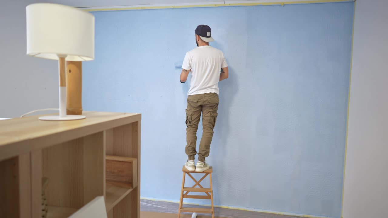 不知名的白人杂工用浅蓝色油漆粉刷墙壁视频下载