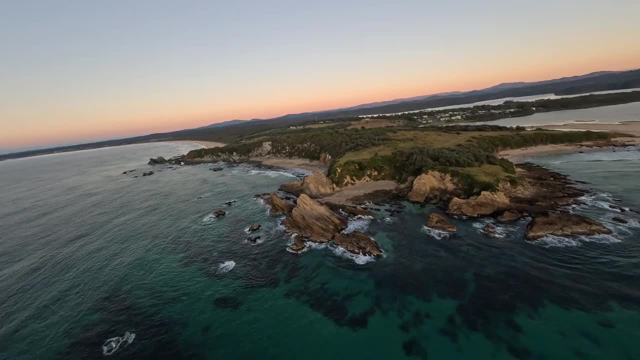 日出时海浪冲击岩石的鸟瞰图。视频下载