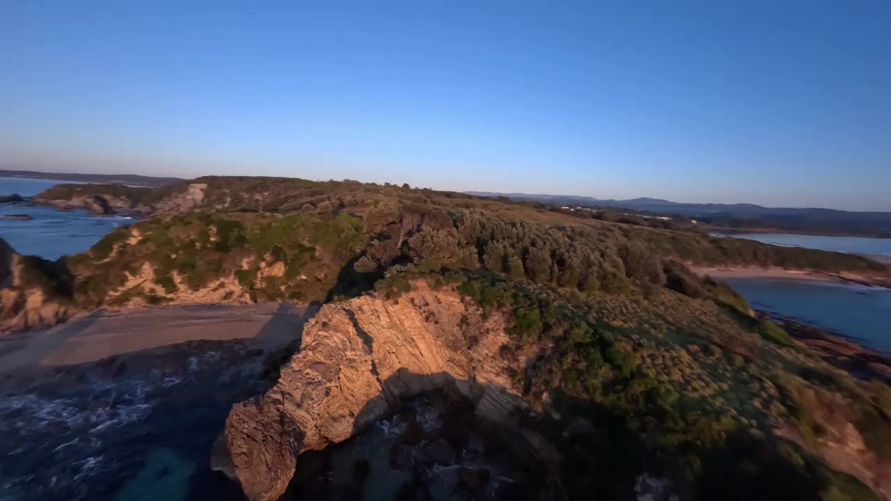 鸟瞰图从日出时站在悬崖顶上的两名游客身边飞过。视频下载