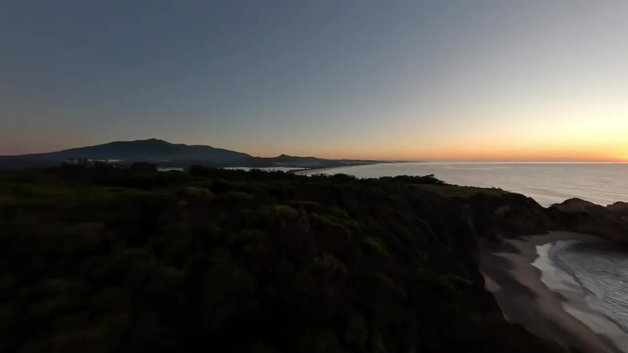 从一个岬角飞过的鸟瞰图，经过两个正在看日出的人。视频下载