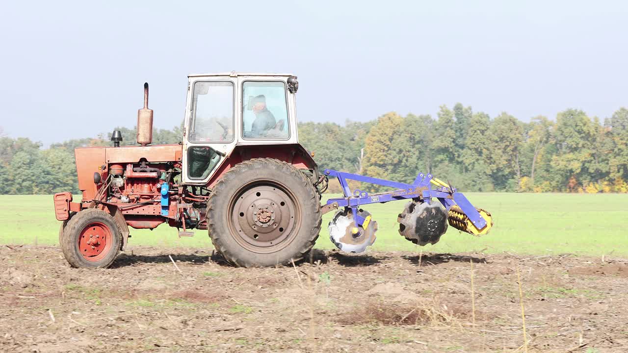 一个成熟的农民在田里开拖拉机干活。视频下载
