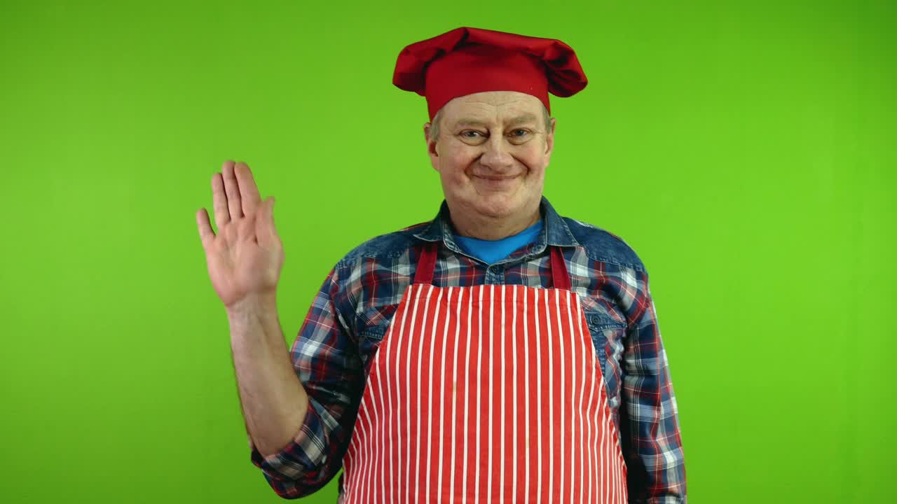 友好的高级厨师在红色围裙挥手致意或告别的手势。视频下载
