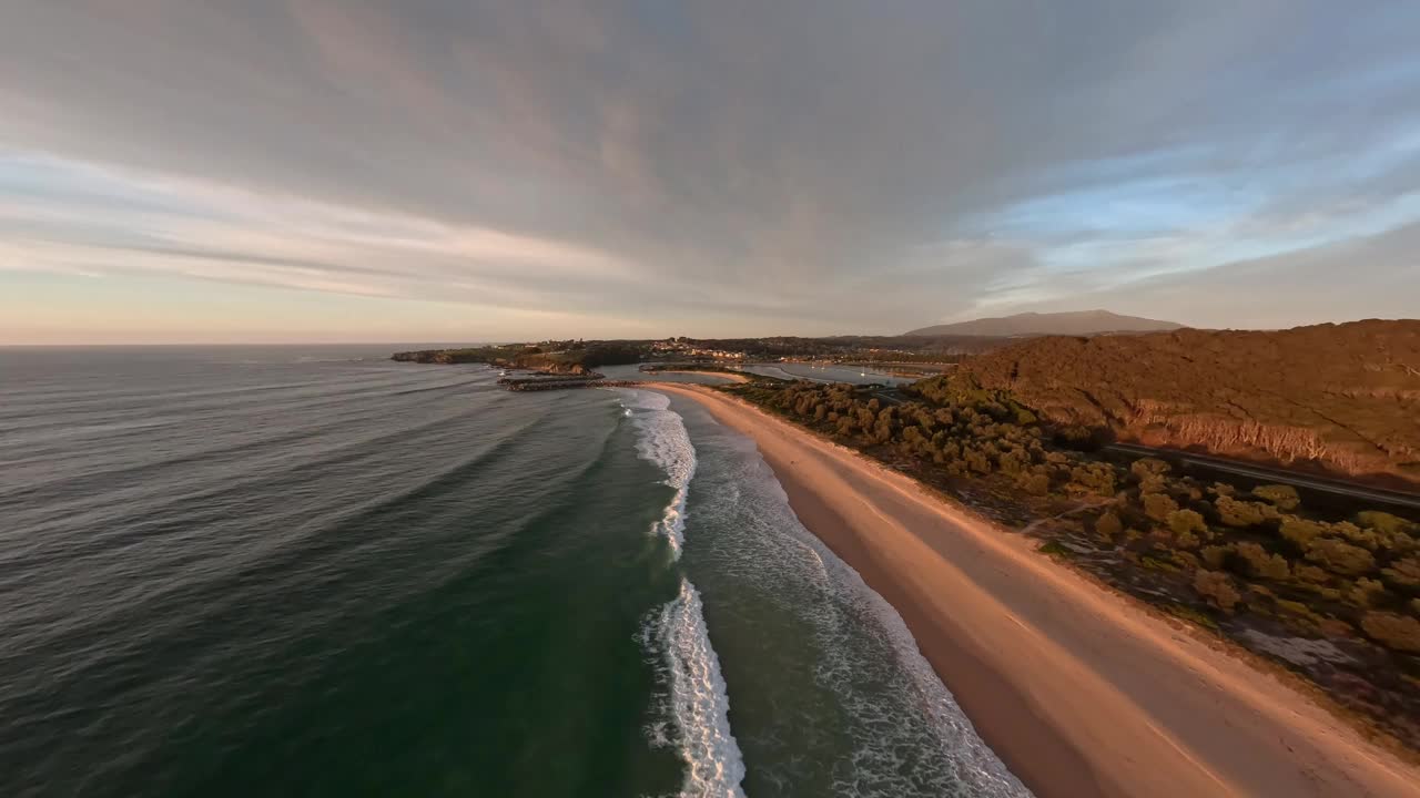鸟瞰在日出时破碎的海浪，冲浪者在水中等待抓住波浪。视频下载