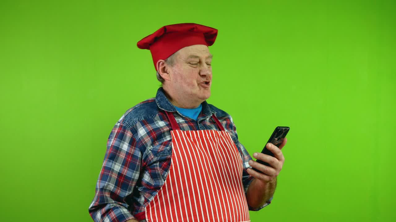 穿着红围裙的高级厨师正在用手机摄像头谈论他生活中的事情。视频下载