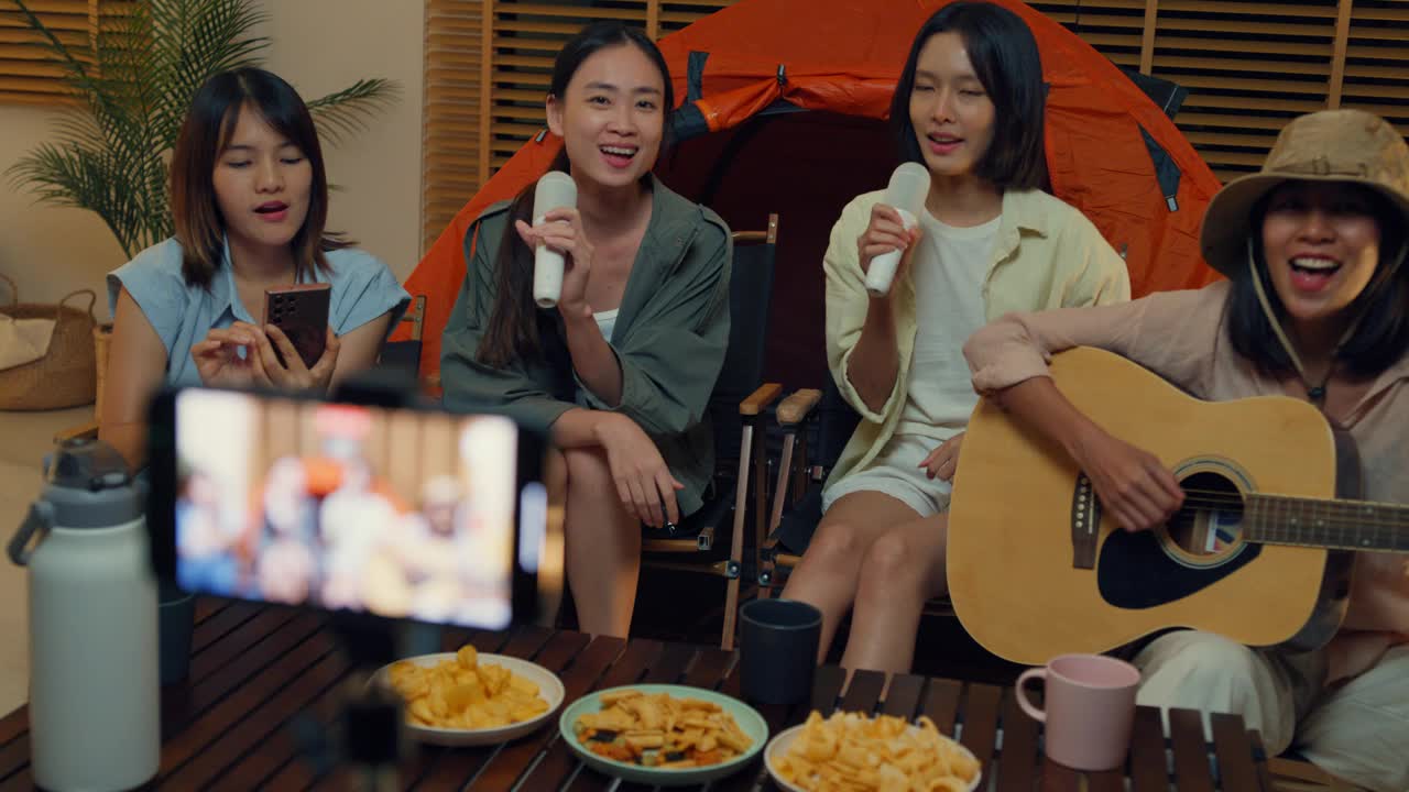 一群亚洲女性朋友晚上在家里的客厅里露营，一边唱歌一边用手机自拍视频通话。快乐的女人边说边笑，享受休闲活动。视频下载